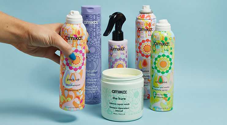 Hand arranging colorful Amika hair care products against a light blue background.