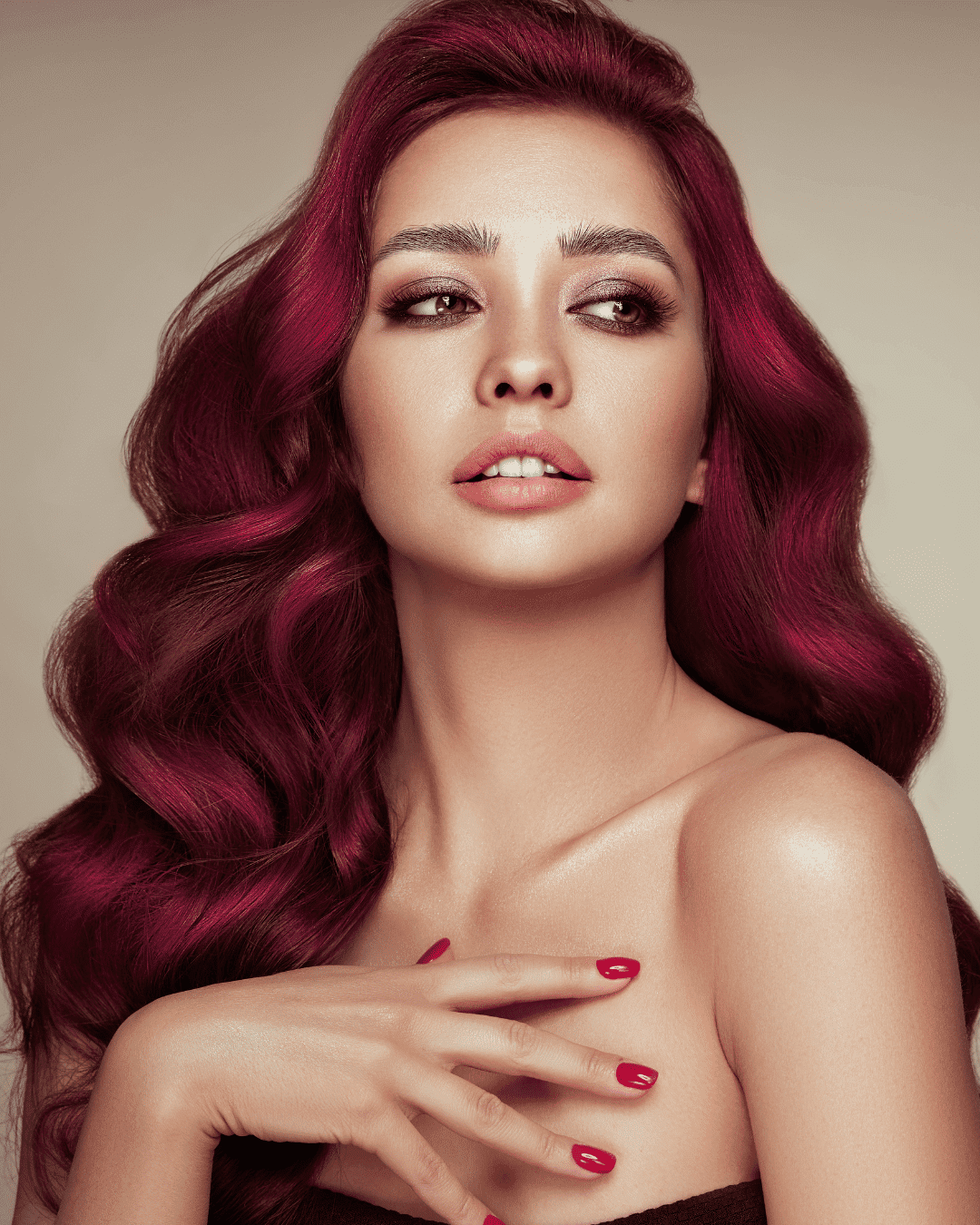Portrait of a woman with long, wavy, vibrant red hair, posing with her hand near her face.