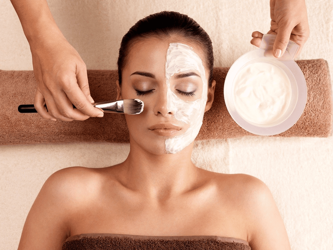 Woman receiving a facial treatment, half of her face covered with a white mask, eyes closed.