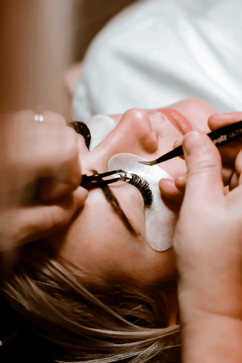 Close-up of a woman getting eyelash extensions by a beauty technician.